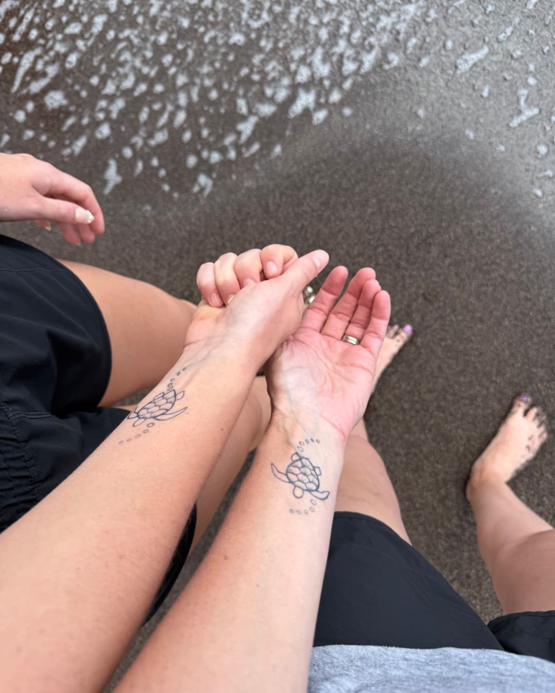 Two people holding hands at the edge of the water.