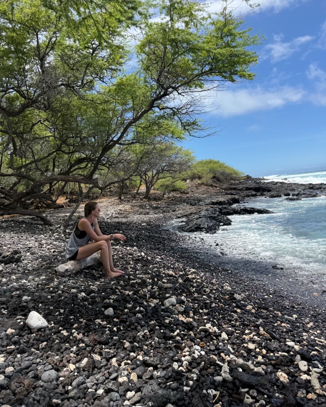 A woman sitting beside the ocean on a rocky beach.