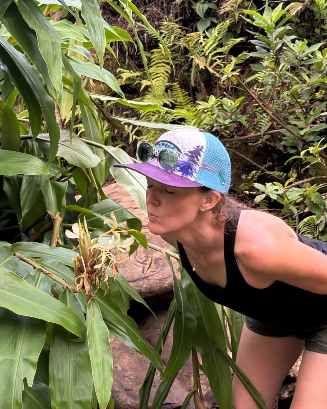 A woman pausing beside flowers and green plants.
